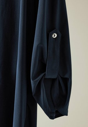 Marineblå langærmet skjorte med struktureret stof. Manchetterne har en knap og en lille læg, som forbedrer det overordnede design.