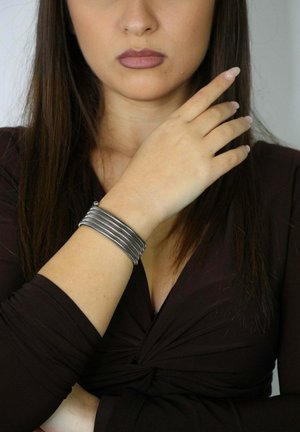 Srebrna bransoletka wielołańcuchowa na nadgarstku, z gładkim metalicznym wykończeniem o delikatnym połysku. Brak widocznego zapięcia, prosty i elegancki design.