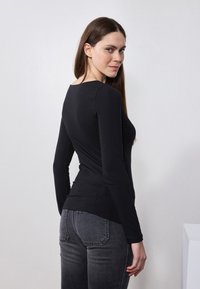 Svart langermet skjorte med en tettsittende design, jevn tekstur og vid rund hals. Kombinert med grå bukser med baklommer.