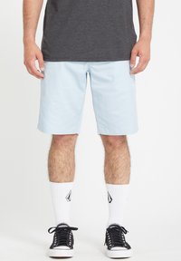 Light blue shorts made of soft fabric, knee-length with a relaxed fit. Paired with black sneakers and white socks featuring a logo.