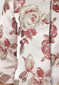 Tela rosa con patrones florales bordados en tonos rojos y beiges, con hojas detalladamente elaboradas, creando textura y profundidad.