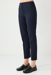 Marineblauwe, op maat gemaakte broek met een slanke pasvorm, voorzien van een glad front, zijslits bij de zoom en een lichtgewicht, gladde stof. Gecombineerd met zwarte loafers.