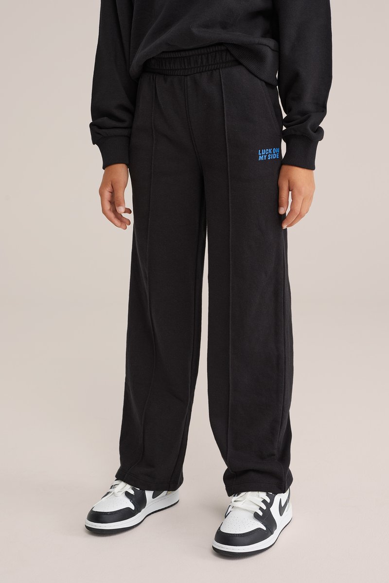 Mustad mustre on elastse ja sinise tekstiga, kus on kirjas "LUCK ON MY SIDE." Kangas on pehme, lõige on mugav ja otse jalad.