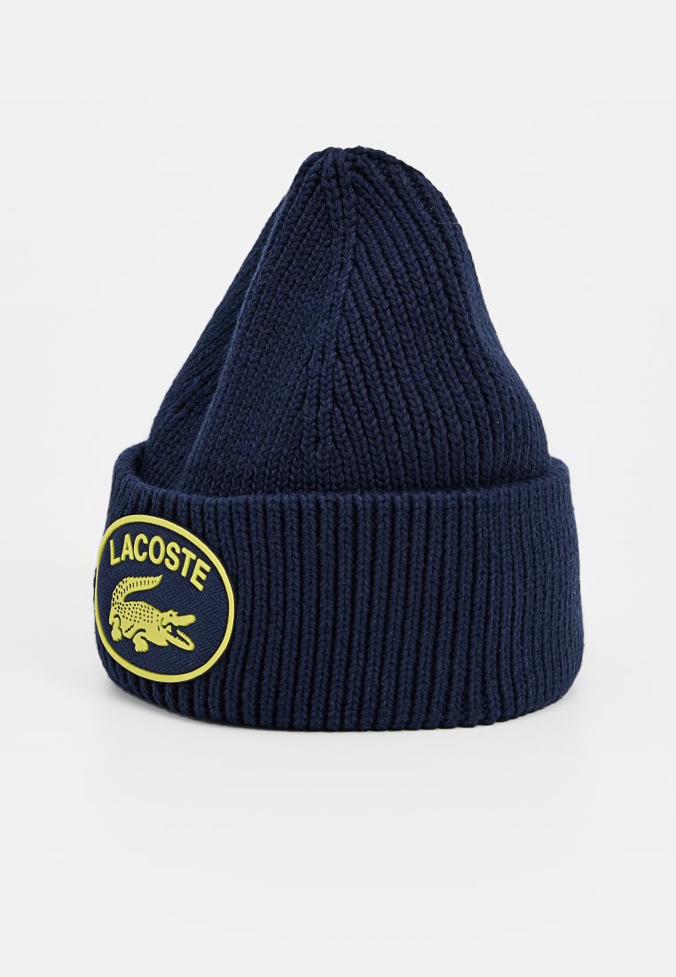 Navy gestrickte Mütze mit Rippstruktur, die ein auffälliges gelbes Lacoste-Logo-Patch mit einem Krokodilmotiv zeigt.