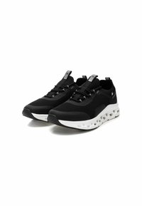 Zapatillas deportivas negras con parte superior de malla texturizada, suela blanca acolchada y cordones elásticos. Presenta un lazo en el talón para facilitar su colocación.