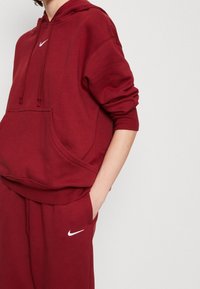 Red hoodie made of soft cotton blend, featuring a kangaroo pocket, ribbed cuffs, and embroidered white Nike logo on the chest.