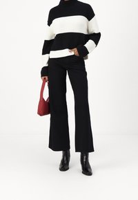 Maglione a righe bianco e nero con collo alto, abbinato a pantaloni neri svasati e una piccola borsa rossa. Stivali neri alla caviglia completano il look.