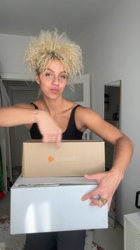 Două cutii de livrare, una maro cu logo-ul Zalando și cealaltă albă. Fundalul arată o cameră cu o oglindă și pereți de culoare deschisă.