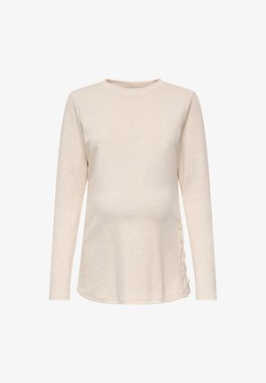Beiges Umstandsoberteil mit langen Ärmeln, rundem Ausschnitt und seitlichen Knopfdetails vor weißem Hintergrund.
