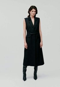 Vestido de casaco preto sem mangas com colarinho em bico, corte ajustado, bolsos laterais e um cinto combinando, feito de tecido suave e estruturado.