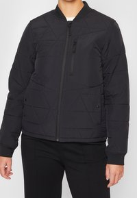 Svart vadderad bomberjacka med dragkedja framtill, ståkrage och sidofickor. Avslutad med textilmaterial och ribbade muddar.