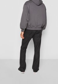 Grijze hoodie met een losse pasvorm, geribbelde boorden en een kangaroezak, gecombineerd met donkerblauwe spijkerbroek en witte sneakers.