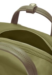 Olivgrön mjuk tygryggsäck med ett slätt läderhandtag. Utrustad med ett dragkedjefack och en kontrasterande inredning.