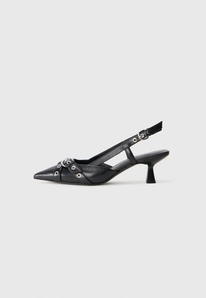 Chaussure slingback en cuir noir avec un bout pointu, des sangles décoratives avec œillets en métal et un petit talon carré. Surface texturée.