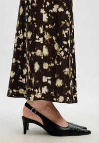 Nedre ben som bär en svart och beige blommig kjol tillsammans med svarta slingback kitten heels med sidspänne.