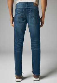 Slim-fit blauwe denim jeans met een gladde textuur, twee achterzakken en subtiele vervagingdetails. Heeft een leren patch bij de taille.