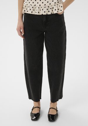 Femme portant un jean noir court avec ourlets bruts, un haut beige à pois avec volants, et des chaussures Mary Jane vernies noires.
