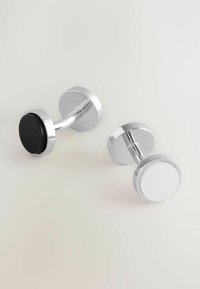 Pair of cufflinks featuring a brushed silver finish with a round black and white design. Smooth texture and circular shapes complement each other.