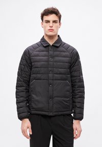 Fekete párnázott dzseki steppelt textúrával, pattintós gombokkal és gallérral. Hosszú ujjú, elől mellzsebbel, amely folttal díszített.