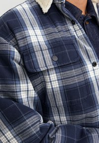 Mörkblå rutig skjorta med vita ränder, lättviktsmaterial, med två bröstfickor, knäppning med knappar och en mjuk, beige fleecekrage.