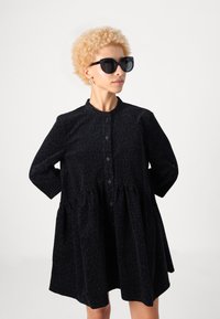 Melna dzīvnieku raksta kleita ar garām piedurknēm, pogu priekšpusi un savāktu jostasvietu. Komplektā ar lielām melnām saulesbrillēm.