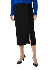 Zwarte wikkelrok met een zijsplit, gemaakt van een soepele stof. Gepaard met een blauwe gebreide cardigan en zwarte puntige hakken.