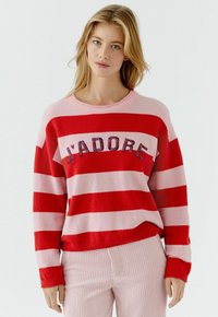 Roter und rosa gestreifter Pullover mit gerippter Textur, mit der Aufschrift "J'ADORE" in mehrfarbigen Buchstaben auf der Brust. Lange Ärmel, rundhalsausschnitt.