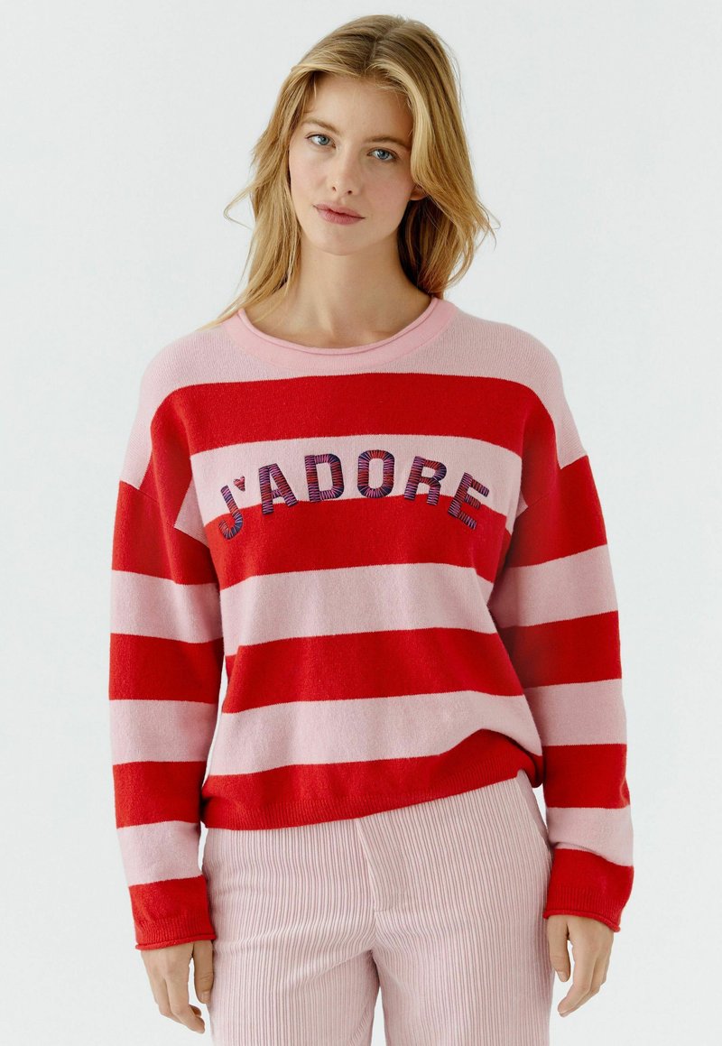 Roter und rosa gestreifter Pullover mit gerippter Textur, mit der Aufschrift "J'ADORE" in mehrfarbigen Buchstaben auf der Brust. Lange Ärmel, rundhalsausschnitt.