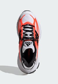 Adidași de alergare cu un superior din plasă albă, accente negre și suprapuneri strălucitoare de portocaliu. Prezintă un guler căptușit și șireturi negre.