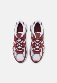 Scarpe da allenamento rosse e bianche con upper in mesh e suede. Presentano lacci bianchi spessi, colletto imbottito e dettagli grigi. Design con punta arrotondata.