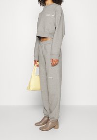 Grå kortärmad sweatshirt med en ficka fram, tillsammans med grå sweatpants med två dragkedjeficks. Bär en gul handväska och har på sig bruna klackstövlar.