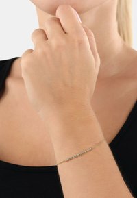 Bracciale in oro con una sottile barra che presenta pietre multicolori. Le pietre sono disposte in linea retta lungo la catena.