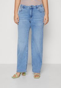 Light blue wide-leg jeans with a button closure and front pockets, paired with green block-heeled sandals and a striped top.