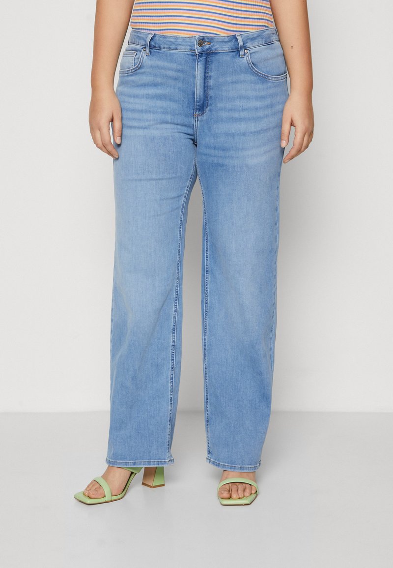 Light blue wide-leg jeans with a button closure and front pockets, paired with green block-heeled sandals and a striped top.