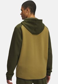 Sweat-shirt à capuche en vert olive et khaki, présentant un design à deux couleurs avec un tissu texturé et une coupe décontractée.