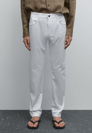 Weiße gerade Hosen aus einem Baumwollmischgewebe. Mit zwei vorderen Taschen, einem vorderen Knopfverschluss und einem schlichten Design.