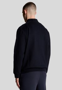 Felpa blu navy con colletto alto, polsini e orlo a costine, texture morbida e design minimalista. Presenta una schiena semplice senza motivi.