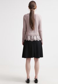 Maglione a maniche lunghe rosa chiaro con bordi in pizzo sul fondo, abbinato a una gonna nera al ginocchio. Tessuto morbido e design aderente.