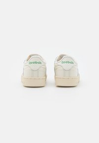 Pair of off-white Reebok sneakers with beige soles viewed from the back, featuring green Reebok logo on heel tabs.