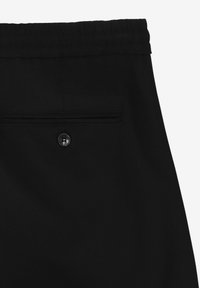 Czarne spodnie wykonane z gładkiego materiału, z elastycznym pasem oraz tylną kieszenią z okrągłym czarnym guzikiem i poziomym otworem.