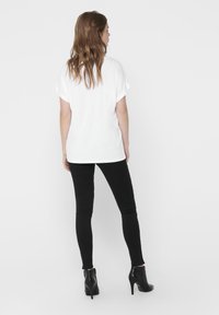 Hvit, kortermet topp kombinert med tettsittende sorte jeans og sorte ankelstøvler. Glatt stoff, avslappet passform, og oppbrettede ermer er synlige.