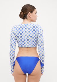 Long-sleeve swim top with a blue and white flower pattern, paired with plain blue bikini bottoms. Material appears smooth and stretchy.