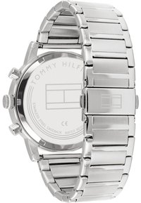 Montre en acier inoxydable argenté avec un bracelet poli, un boîtier rond, des fonctionnalités de chronographe et un dos de boîte transparent affichant les détails de la marque.