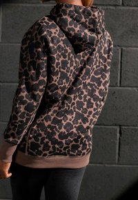 Sweat à capuche imprimé léopard présentant un tissu doux, des couleurs marron et noir atténuées, une capuche avec cordon de serrage, ainsi que des poignets et un ourlet côtelés.