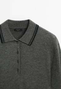 Polo en maille gris foncé avec des doubles rayures noires sur le col et quatre boutons noirs sur le devant.