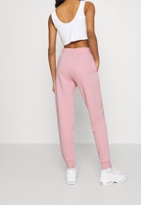 Light pink sweatpants with a relaxed fit, elastic waistband, and side pockets, paired with a white sleeveless crop top and white sneakers.