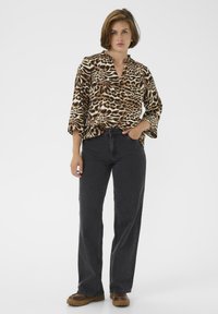 Tijgerprint blouse met een v-hals, 3/4 mouwen, gecombineerd met hoge zwarte jeans en bruine klompen, met een relaxte pasvorm.