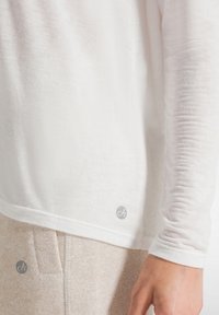 Top bianco a maniche lunghe realizzato in tessuto leggero, con una superficie leggermente strutturata e un accento con il logo vicino all'orlo.