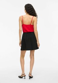 Röd spaghetti-ärmad topp parat med en svart plisserad miniskirt. Slät tyg, figurnära design och böjd sidsöm. Svarta klacksandaler.