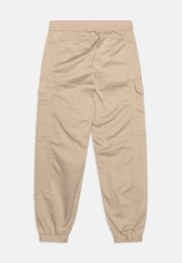 Beige cargo kalhoty s elastickým pasem, zúženými manžetami a bočními kapsami. Látka vypadá měkká s minimální texturou a jednoduchým designem.